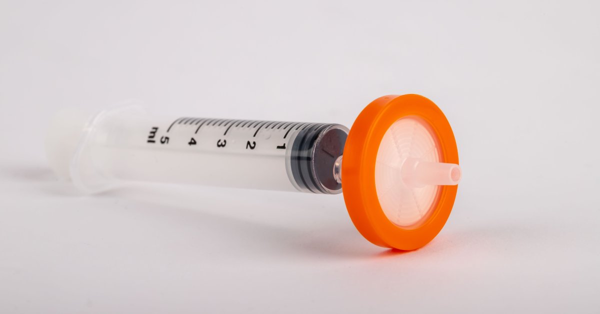 A syringe filter with an orange cap. The plastic syringe has black numbers measuring milliliters.