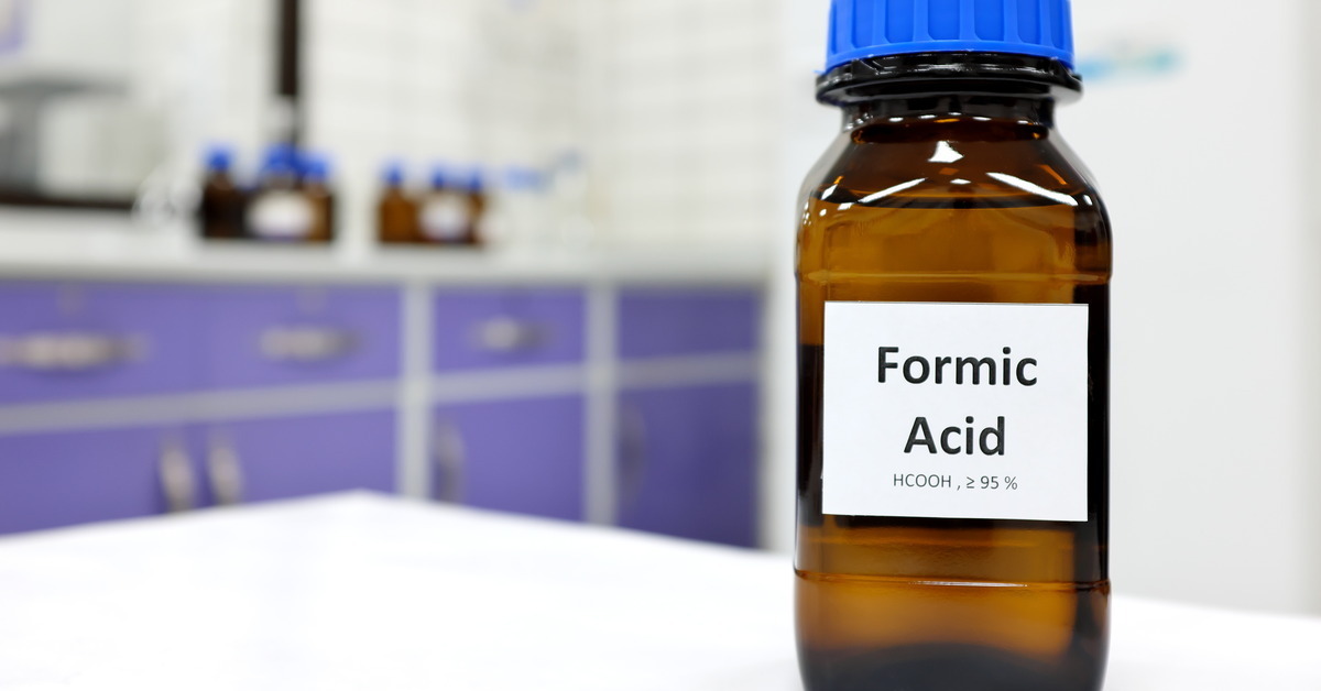 Close-up to a small brown glass bottle with a blue cap and a large white label displaying the words 'formic acid'.