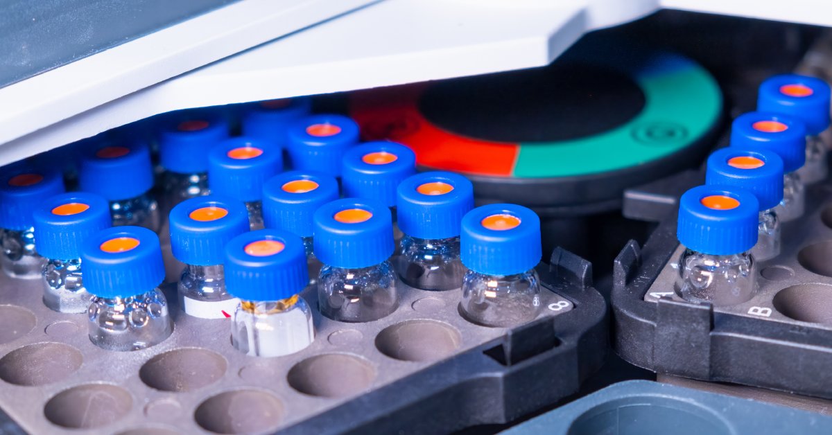 Multiple lab vials, each with a blue cap with an orange septa, are shown full of gel. The vials are on two trays in an autosampler machine.