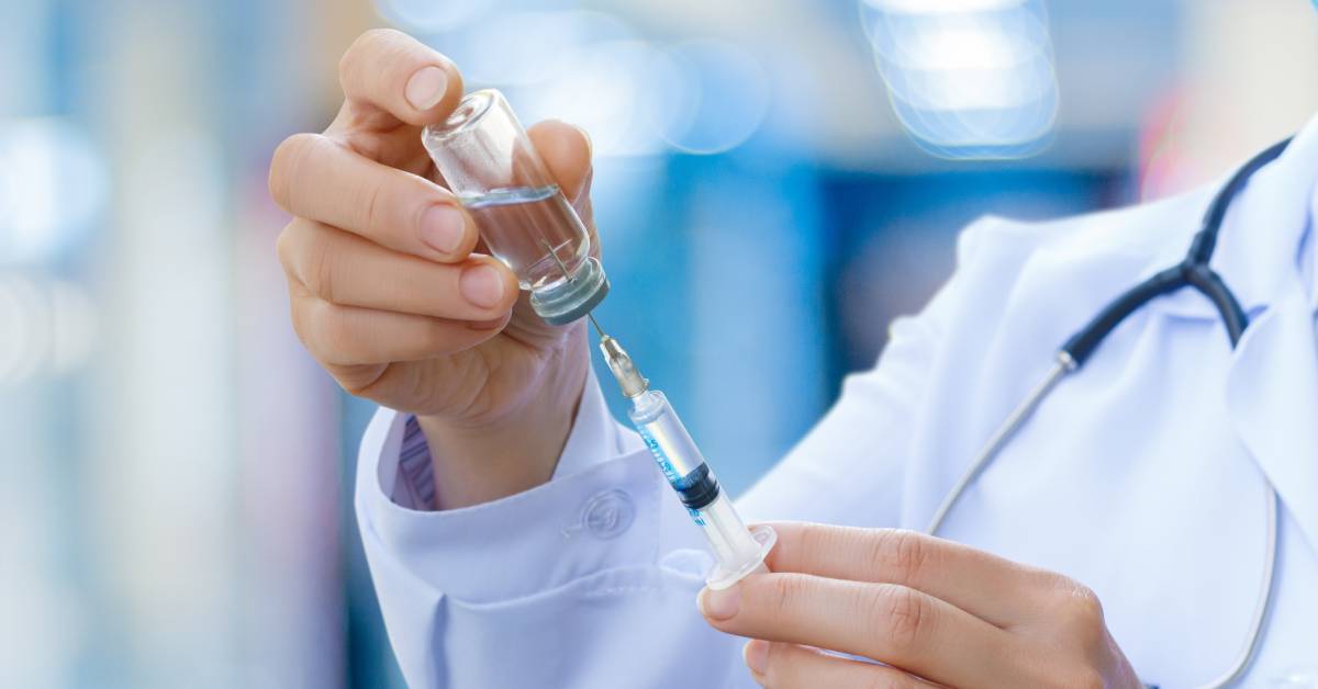 A doctor with a stethoscope holding a syringe and filling it up with a clear liquid from a vial.